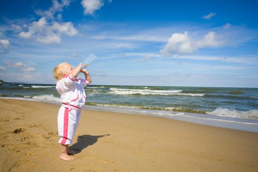 Little girl standing on coastline and drinking water