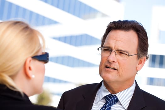 Attentive, Handsome Businessman in Suit and Tie Talking with Female Colleague Outdoors.