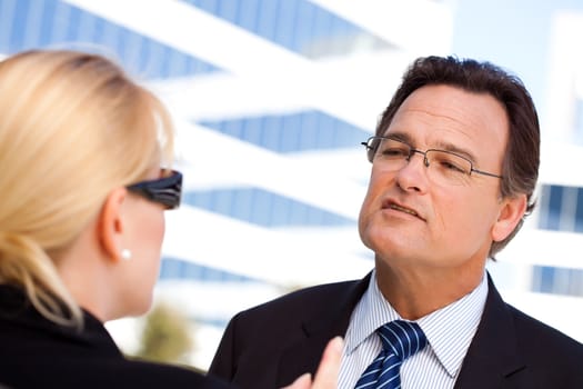 Attentive, Handsome Businessman in Suit and Tie Talking with Female Colleague Outdoors.