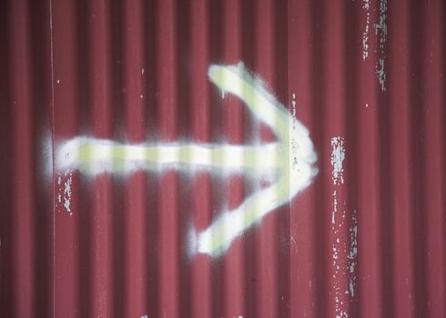 Spray-painted arrow on red corrugated surface.
