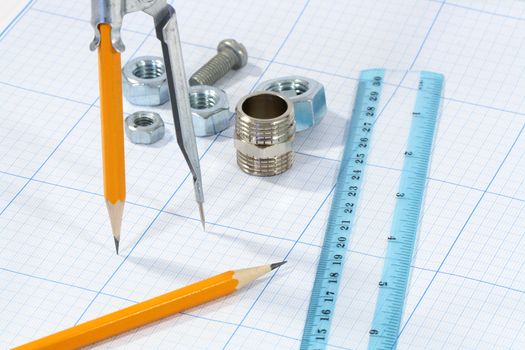 Divider, pencil, ruler and few screw nuts on graph paper background