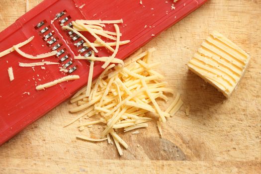 Closeup of grated cheese and grater lying on wooden cutting board