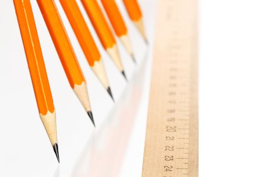 Few wooden yellow pencils in a row and ruler on white background