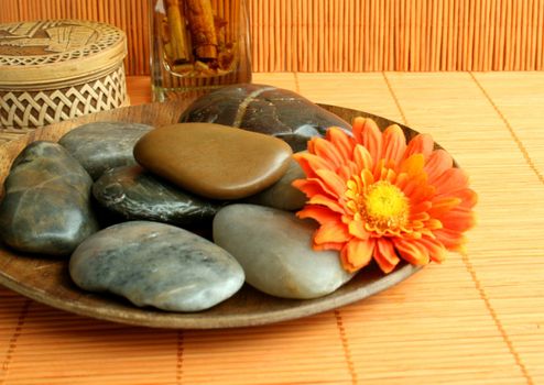 Stones lay on a brown plate and a bright flower