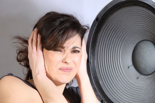Stressed woman holds in front of a large speaker to the ears