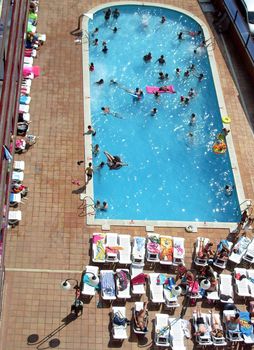 Sunbathers on patio by swimming pool in Spanish tourist hotel.