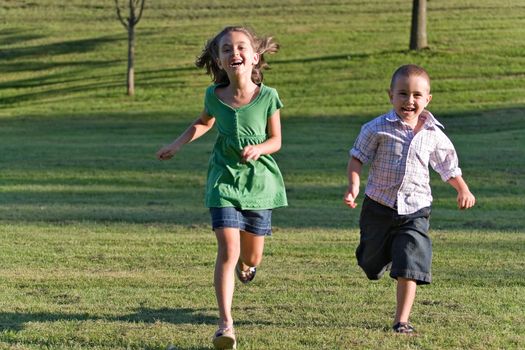 Two happy little kids having fun while running through the grassy field and racing against each other.