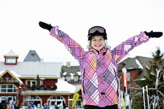 Happy teenage girl with arms raised in ski helmet at winter resort