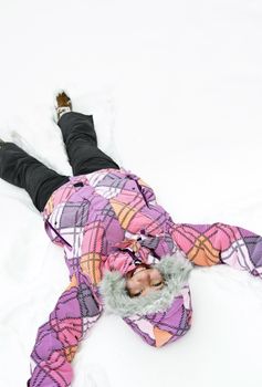 Happy teenage girl making snow angel in winter