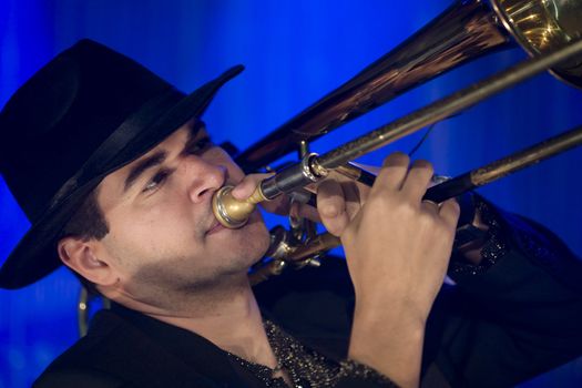 A trombonist in a black suit and blue background.