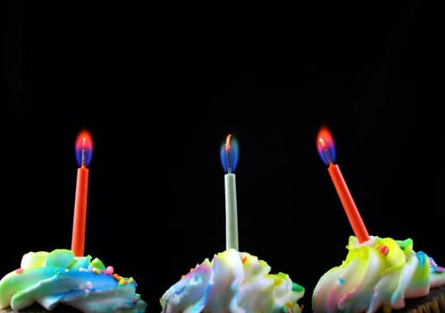 cupcakes lined up with candles on a black background. Candles are the main objects.


