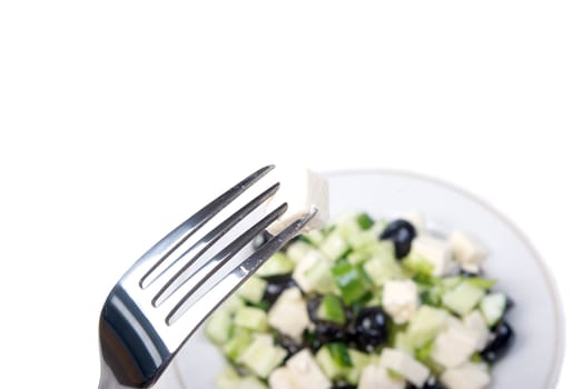 fork with cheese and greeak salad on a plate.