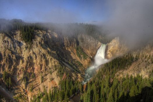 A waterfall flowing into a canyon with clouds and fog. Shot in HDR.