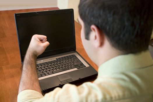 A young business man getting frustrated with his laptop.  He could also be happy at what he is seeing.  Plenty of copy space on the screen.