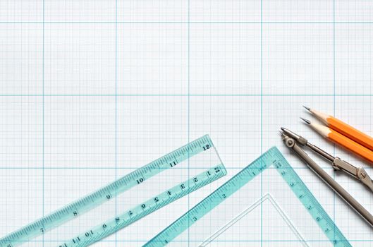 Divider, pencils and rulers on blue graph paper background