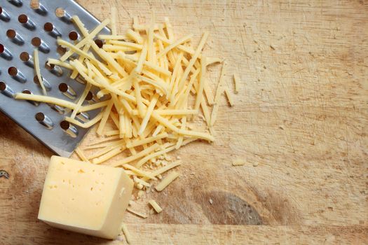 Closeup of grated cheese and grater lying on wooden cutting board