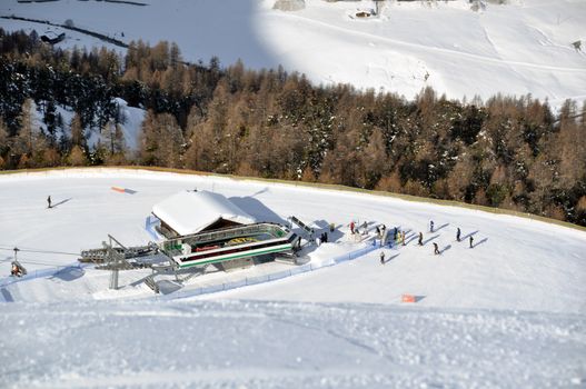 View down on lower station of modern chairlift with trees and huts down in the valley in the background - shot in Livigno, Italian Alps