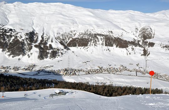 View down on lower station of modern chairlift with trees and a village down in the valley plus immense mountains in the background - shot in Livigno, Italian Alps