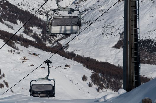 Chairlifts with ski slopes and skiers in the background - shot in Livigno, Italian Alps