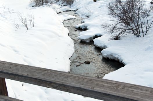 Creek running through snow covered banks and wooden rail of a bridge