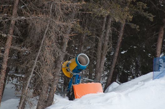 Snow making machine located at the border of the skiing slope in front of a forest. Shot in Livigno, Italian Alps