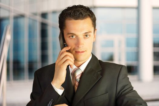 Close-up portrait. Businessman outside a modern building with phone.