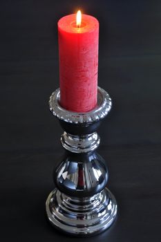 Burning red candle in silver holder on dark wooden table