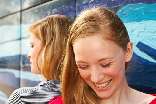 outdoor portrait of two laughing girls next to a painted wall