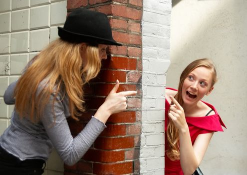 Two girls peeking around the two sides of the wall at house entrance