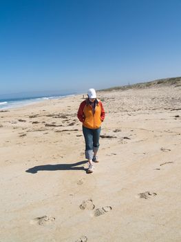 Woman walking on the beach, with dunes in the background.