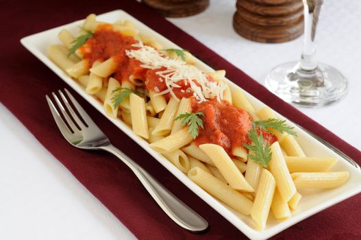 Plate of penne pasta with tomato sauce and fresh herbs.