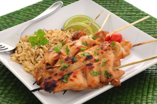 Chicken skewers served with rice and tomatoes.
