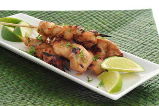Grilled chicken satay served with lime wedges.