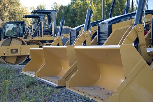 New yellow bulldozers in a row with buckets and rollers.