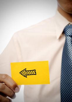 Arrow in yellow card showing direction holding by businessman.