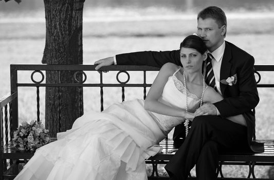 Newlywed couple relaxing on bench in black and white portrait.