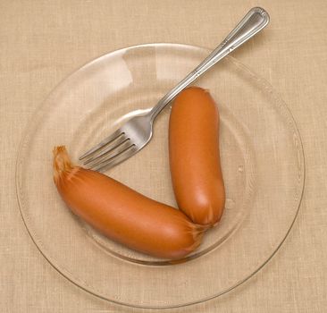 Sausages and a fork on a transparent plate.