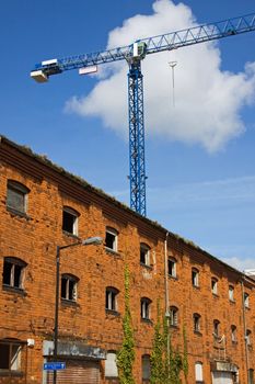 A tower crane on an inner city construction site dominates a dilapidated warehouse in Bristol