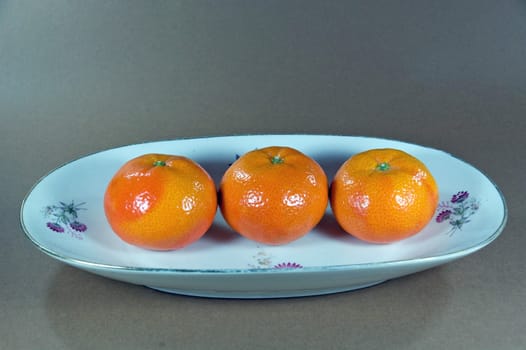 primer plano de tres mandarinas en un plato con fondo gris