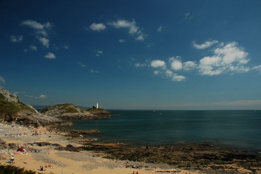 Swanse beach and rock with white lighthouse, sea and blue sky