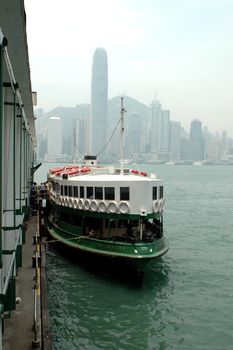 Hongkong ferry pier with old ferry passing harbour. Behind, far away - modern skyscrapers.