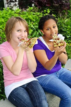 Two teenage girls sitting and eating pizza