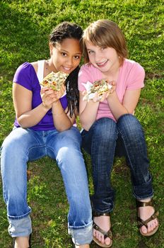 Two teenage girls sitting and eating pizza