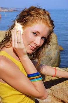beautiful girl holds a seashell close to the ear