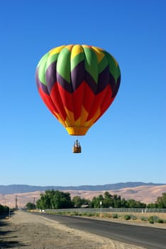 A multi colored Hot Ait Balloon coming in for a landing.