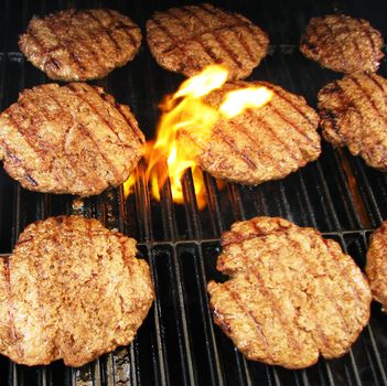 Cooking hamburgers on a grill with flames.

