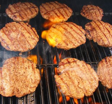 Cooking hamburgers on a grill with flames.
