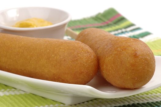 Golden corndogs on a plate with mustard.
