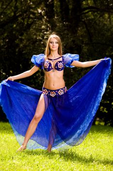 Lovely young woman dancing belly dance in blue outdoors