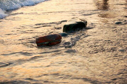 stones at sea shore covered with film of flowing water at sunset